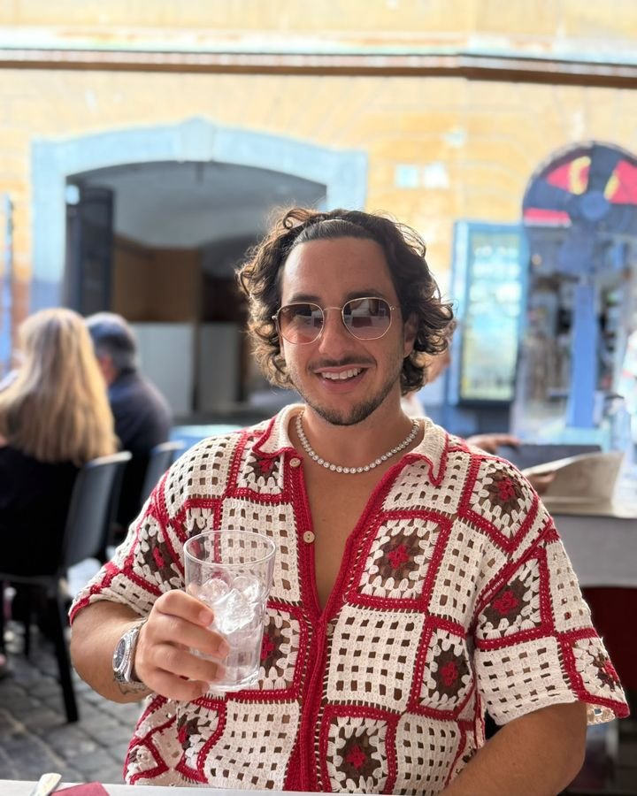 Cristian Ramírez en una terraza, con camisa de ganchillo y un vaso en la mano
